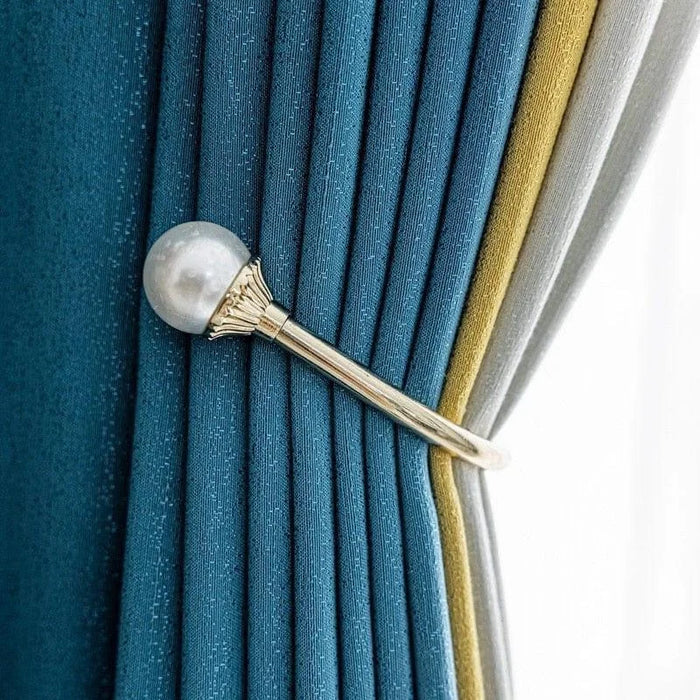 Attache-rideau élégant avec perle décorative, tenant des rideaux de couleur bleu, jaune et gris dans un style raffiné pour une décoration intérieure moderne et chic. Accessoire idéal pour ajouter une touche sophistiquée à votre salon ou chambre.