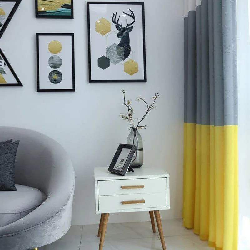 Voici une suggestion de texte alternatif :
"Salon moderne avec canapé gris, meuble d'appoint blanc à pieds en bois, rideaux bicolores gris et jaunes, et décorations murales géométriques. Vase élégant avec branches fleuries apportant une touche naturelle."