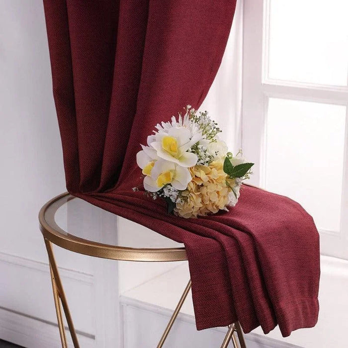 Rideau élégant rouge bordeaux drapé sur une table en verre avec bouquet de fleurs blanches et jaunes, idéal pour un salon chic et moderne. Accessoire décoratif pour embellir votre intérieur et créer une ambiance chaleureuse et accueillante. Fenêtre en fond laissant entrer la lumière naturelle.