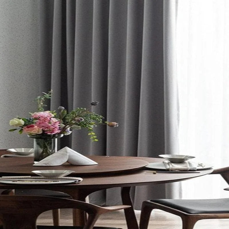 Table à manger élégante avec décoration florale et chaises modernes en bois, située près d'un rideau gris chic. Cette salle à manger raffinée crée une ambiance conviviale et chaleureuse idéale pour les repas en famille ou entre amis, ajoutant une touche de sophistication à votre intérieur.