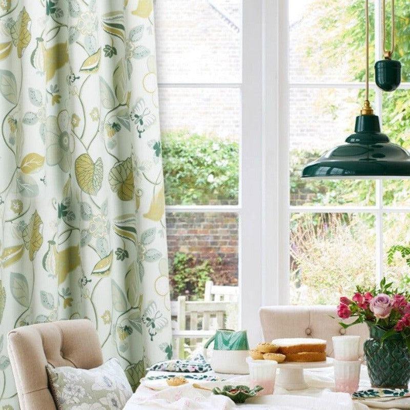 Rideaux à motifs floraux verts et jaunes, ajoutant une touche de fraîcheur et de nature à votre décoration intérieure, suspendus près d'une grande fenêtre laissant entrer la lumière naturelle. Parfait pour illuminer votre salle à manger ou salon, avec un style élégant et accueillant.