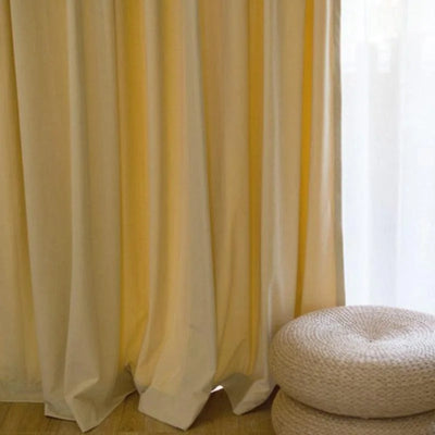 Rideaux élégants de couleur jaune pâle pour salon avec pouf tressé beige sur plancher en bois. Ambiance lumineuse et chaleureuse pour intérieur moderne.