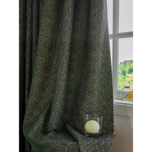 Rideau épais gris foncé drapé dans un intérieur lumineux, accentuant l'élégance d'une pièce. Accessoire déco avec bougie dans son support en verre, créant une ambiance chaleureuse près de la fenêtre ouverte avec vue sur un paysage verdoyant. Idéal pour ajouter une touche sophistiquée à votre salon ou chambre.