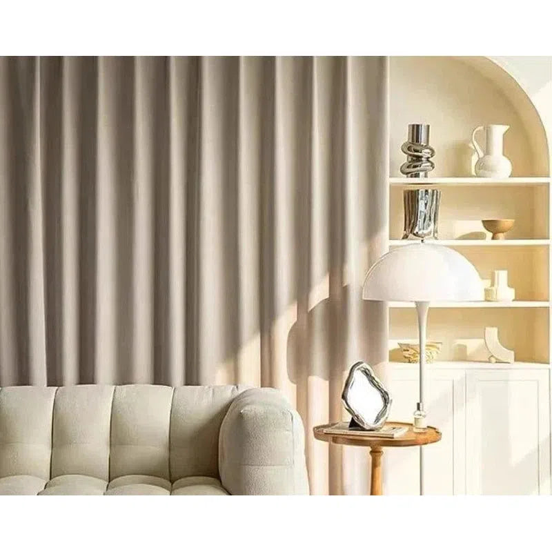 Canapé moderne beige avec rideaux assortis, éclairé par une lampe élégante sur une table en bois. Décoration intérieure contemporaine avec étagères minimalistes. Style épuré et sophistiqué pour un salon confortable.