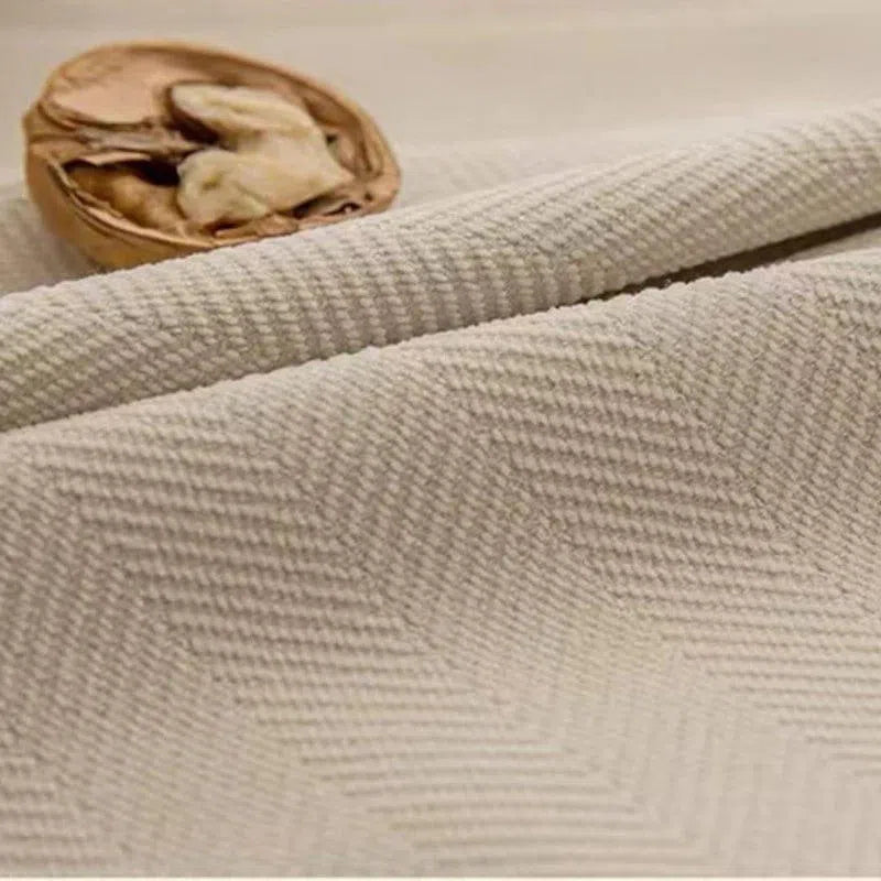 Image d'un tissu beige texturé avec un motif en chevron, idéal pour la décoration intérieure ou la création de vêtements élégants. Le fond neutre met en avant la texture détaillée et ajoute une touche de sophistication à l'ensemble. Un élément naturel complète cette présentation harmonieuse.