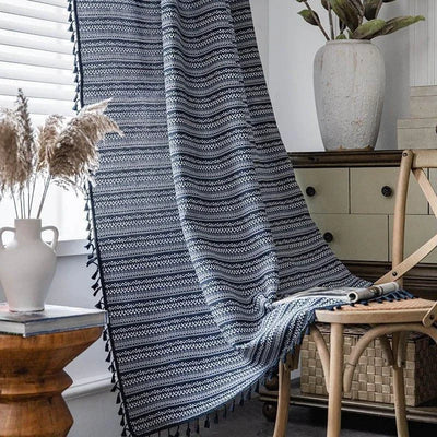 Rideau à motifs géométriques bleu et blanc suspendu près d'une fenêtre lumineuse, créant une ambiance chaleureuse et moderne dans un salon élégant avec des accents naturels. Accessoire décoratif idéal pour habiller vos espaces de vie avec style et raffinement.