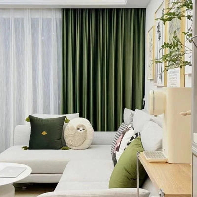 Salon moderne avec rideaux verts, canapé gris clair avec coussins décoratifs. Décoration murale tendance avec cadres, ambiance accueillante et confortable idéale pour se détendre.