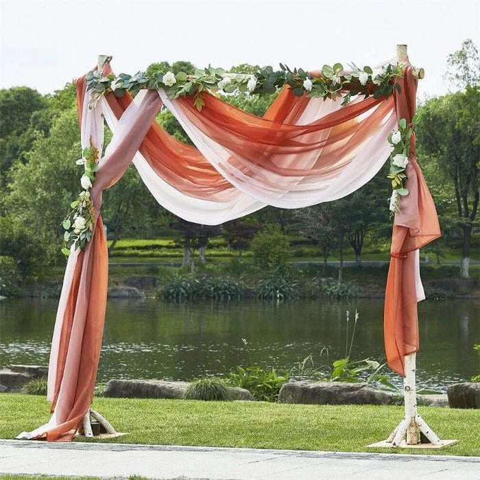 Arche de mariage élégante ornée de drapés aux teintes rose et pêche, décorée de fleurs blanches et de feuillages, idéale pour une cérémonie en plein air. Parfaite pour un cadre romantique et naturel au bord d'un étang.