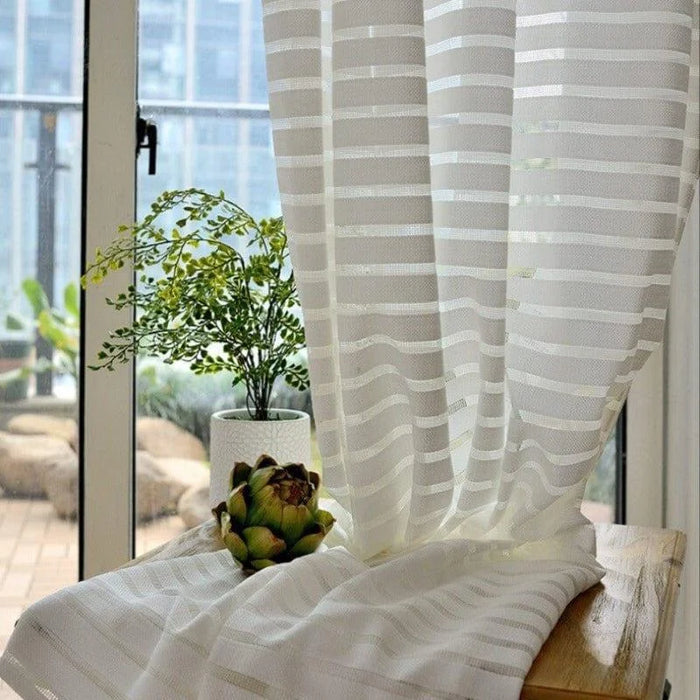 Voilage à rayures blanches filtrant la lumière, idéal pour un salon moderne avec vue sur le balcon. Élégant et pratique, il met en valeur vos plantes d'intérieur tout en créant une ambiance lumineuse.