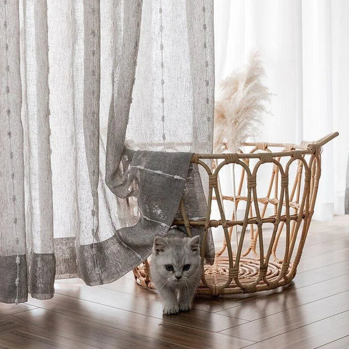 Chaton mignon explorant près d'un panier tressé, décorations modernes de salon, rideaux élégants pour intérieur chaleureux, lumière naturelle tamisée créant une atmosphère accueillante.