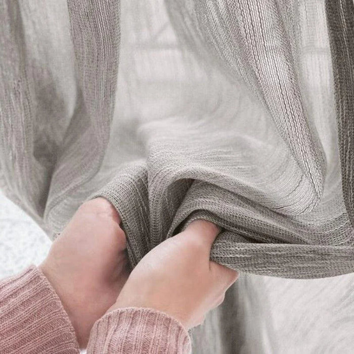Rideau gris élégant accroché, tenu par des mains, parfait pour créer une ambiance chaleureuse et intime. Idéal pour décorer votre salon ou chambre et offrir une touche moderne à votre intérieur.