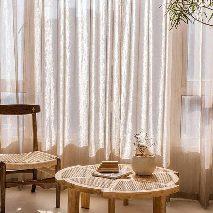 Rideaux légers et élégants habillant une fenêtre, illuminant un coin détente avec une table basse au design épuré et une chaise rustique. Ambiance chaleureuse et accueillante pour une décoration intérieure moderne et naturelle. Plante d'intérieur ajoutant une touche de verdure apaisante.