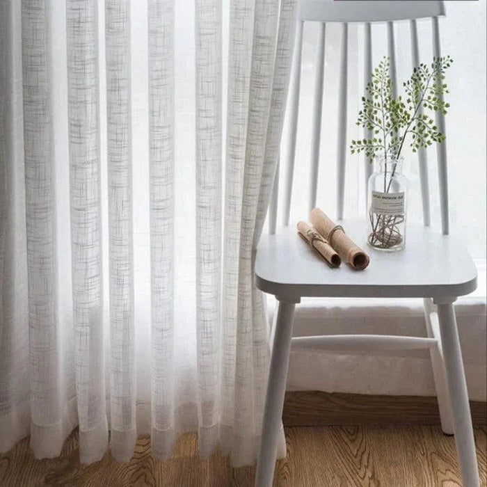 Voilage blanc élégant devant une fenêtre ensoleillée, entouré d'un décor minimaliste avec une chaise blanche et un vase décoratif, créant une atmosphère apaisante et moderne dans la pièce. Idéal pour ajouter une touche de luminosité et de style à votre intérieur.