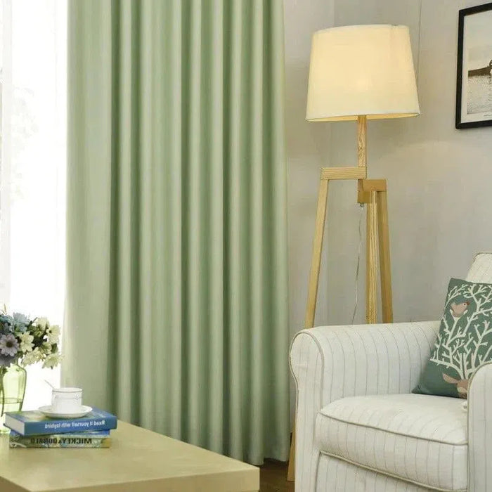 Salon moderne avec rideaux verts, lampe sur pied en bois et fauteuil blanc à rayures fines. Décoration intérieure élégante avec des coussins décoratifs sur le canapé, une table basse avec livres et fleurs en vase. Atmosphère accueillante et lumineuse.