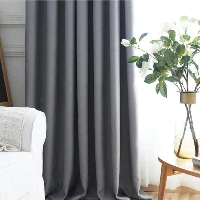 Rideau opaque gris moderne pour salon, idéal pour une décoration intérieure élégante. Complète parfaitement un canapé blanc et un vase sur table en bois. Bloque efficacement la lumière tout en ajoutant une touche de sophistication.