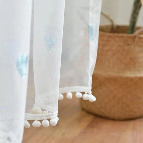 Rideau blanc élégant avec motifs délicats en forme de cœur, idéal pour ajouter une touche raffinée à votre espace intérieur. Finition avec pompons décoratifs pour un charme supplémentaire. Parfait pour la décoration de la chambre ou du salon.
