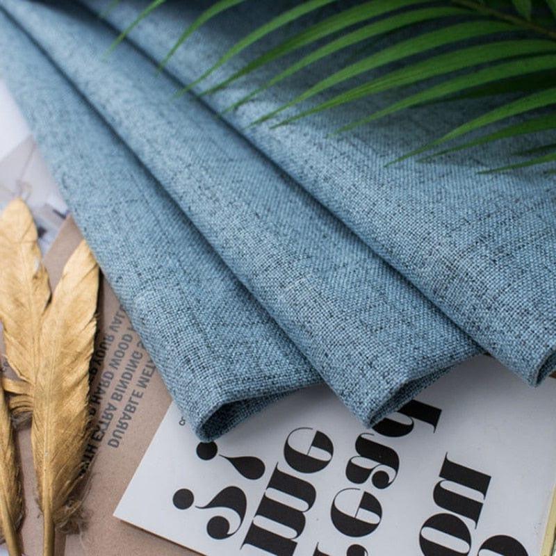 Photo d'un tissu bleu plié, idéal pour la décoration d'intérieur, posé sur des magazines avec des feuilles dorées et une branche verte, créant une ambiance moderne et élégante.