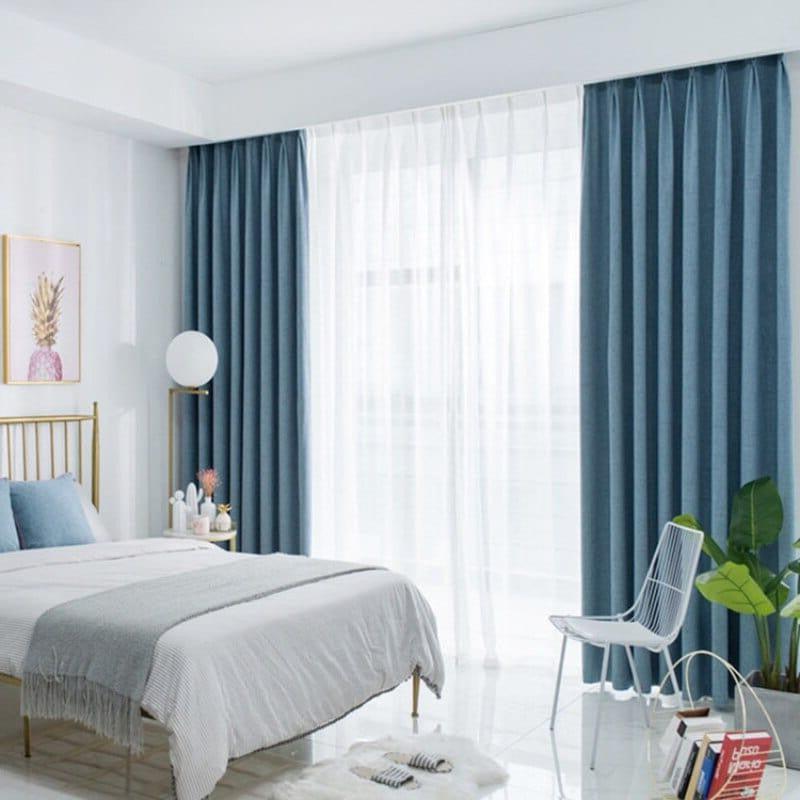 Chambre moderne et élégante avec grande fenêtre équipée de rideaux occultants bleu, décoration intérieure contemporaine avec lit confortable, accessoire de sol et plantes vertes pour une ambiance apaisante. Espace lumineux grâce à la lumière naturelle, idéal pour le repos et la relaxation.