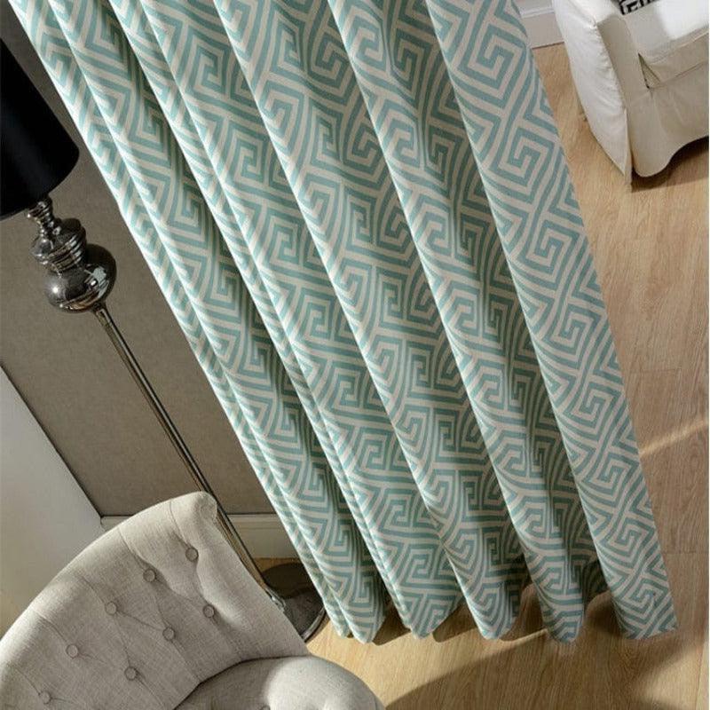 Rideaux à motif géométrique turquoise et blanc pendus dans un salon moderne, accompagnés d'un fauteuil beige et d'une lampe sur pied en métal pour une décoration intérieure contemporaine et élégante.