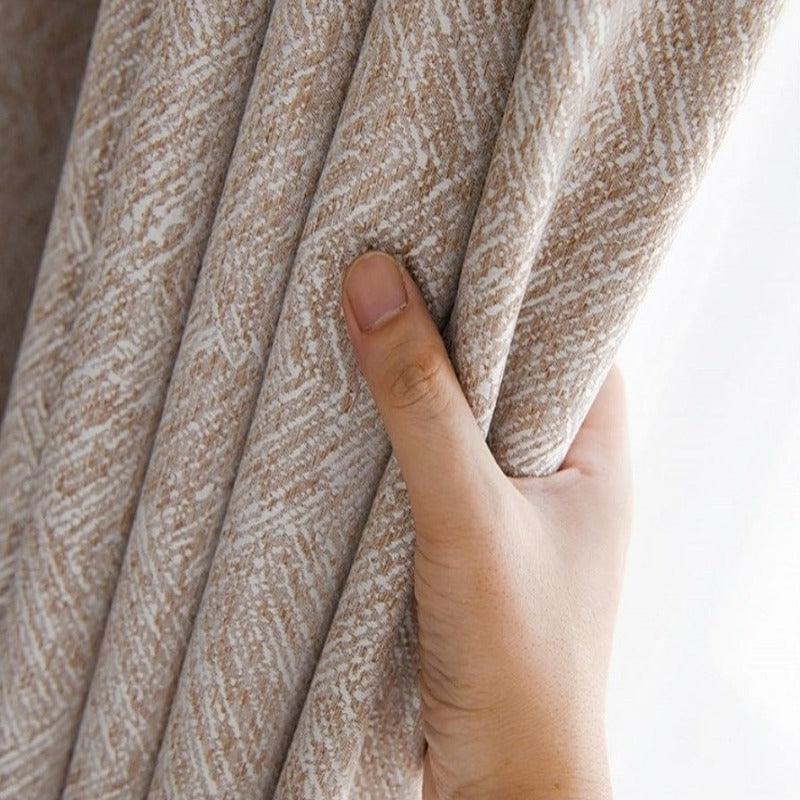 Main tenant un rideau beige texturé, ajoutant une touche élégante et naturelle à votre intérieur. Solution idéale pour un ameublement raffiné et moderne, offrant intimité et style à votre décoration intérieure.