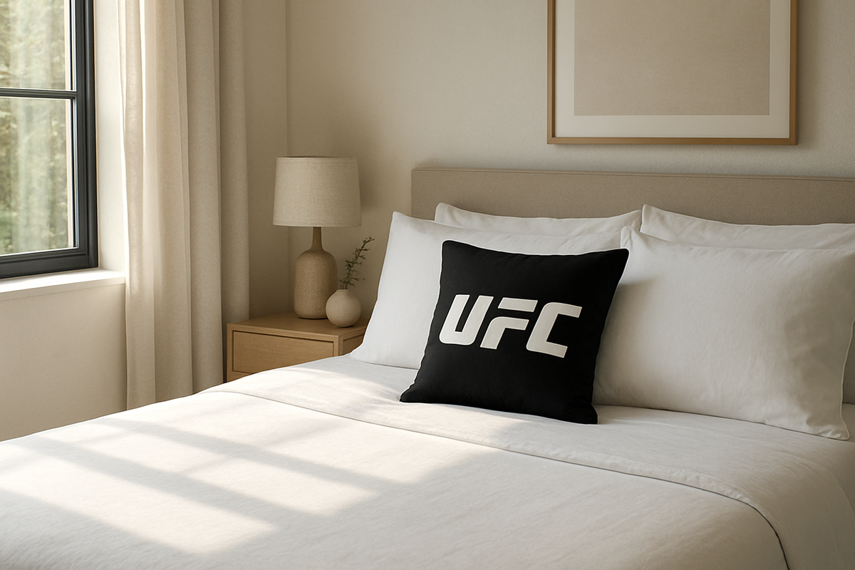 Oreiller UFC officiel en mousse à mémoire de forme posé sur un lit blanc dans une chambre lumineuse, avec logo UFC visible sur la housse