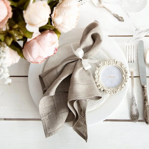 Une élégante table de dîner avec des fleurs de pivoine, une serviette enroulée et un cadre décoratif sur un fond clair.