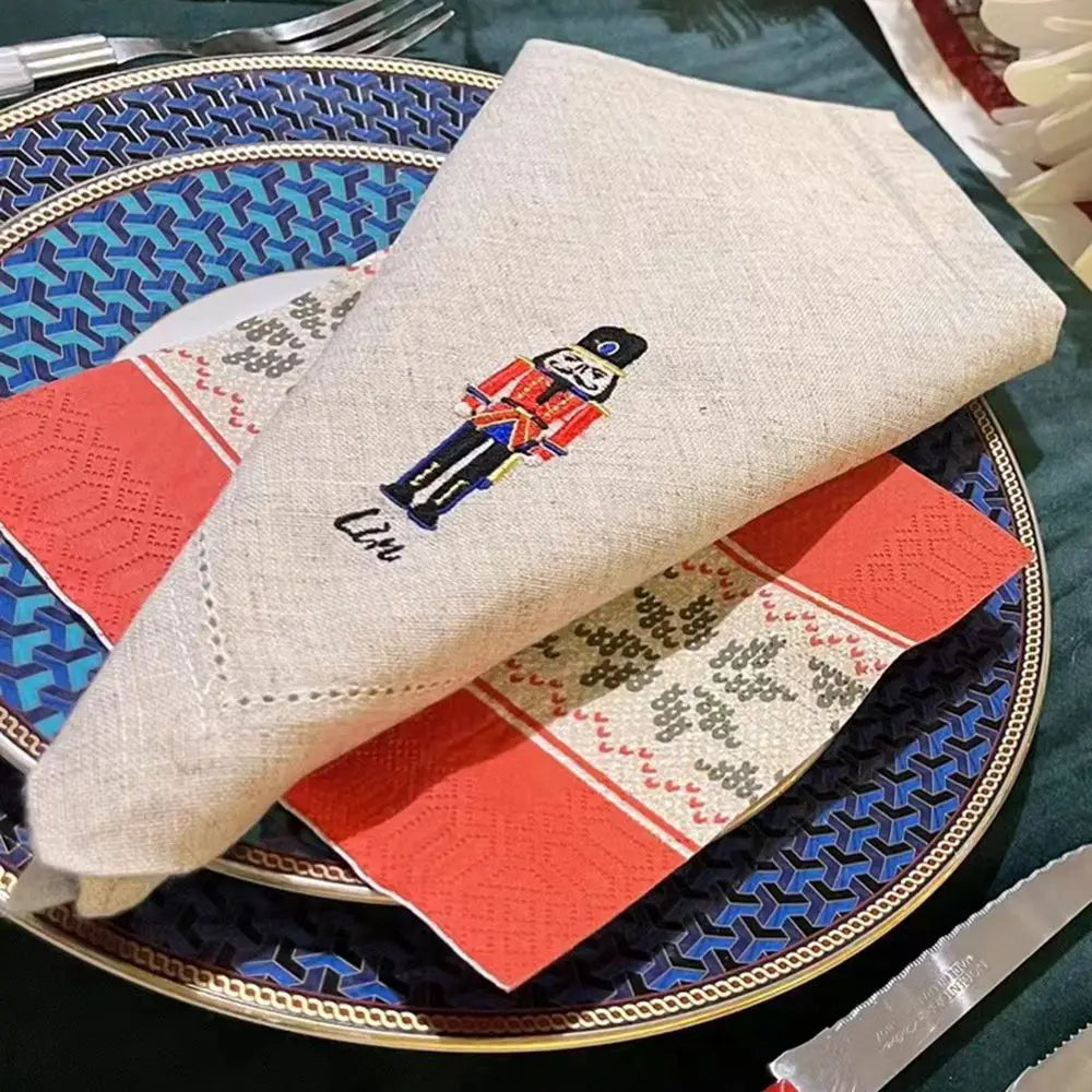 Un étui décoré d'un personnage de soldat en broderie, posé sur une assiette en métal avec des motifs géométriques.