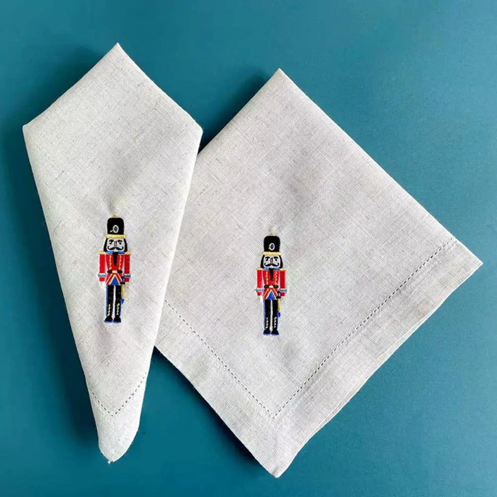 Deux serviettes de table en lin avec des jouets soldats brodés dessus sont posées sur un fond bleu-vert.