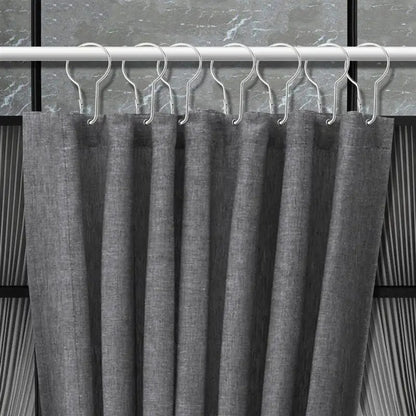 Crochets métalliques fixés à un rideau gris foncé sur une tringle, montrant leur compatibilité avec les rideaux épais.