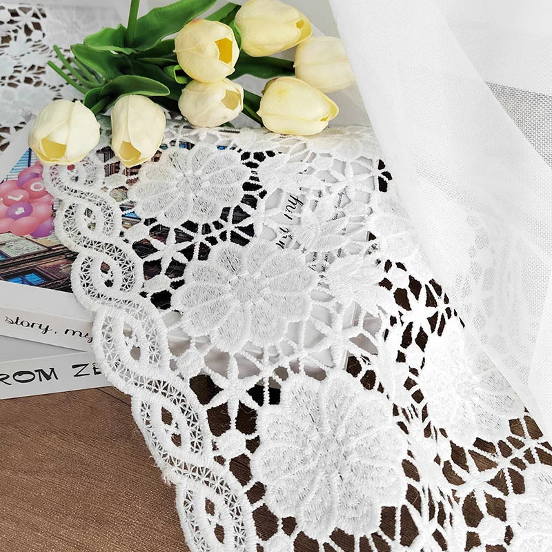 Détail d’un voilage blanc brodé posé sur un livre avec un bouquet de tulipes jaunes pour une ambiance poétique.