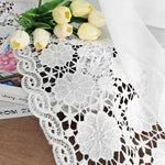 Détail d’un voilage blanc brodé posé sur un livre avec un bouquet de tulipes jaunes pour une ambiance poétique.