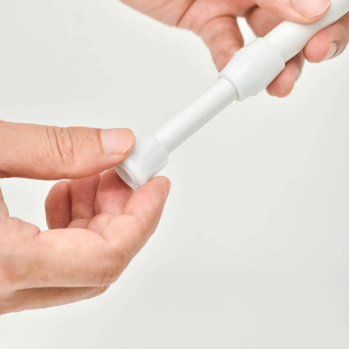 Gros plan sur l'extrémité d'une tringle à rideaux blanche sans perçage, tenue entre deux mains.