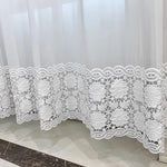 Gros plan sur le bas d’un voilage blanc avec une broderie florale ajourée au motif délicat.