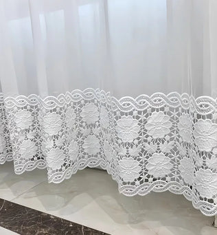 Gros plan sur le bas d’un voilage blanc avec une broderie florale ajourée au motif délicat.