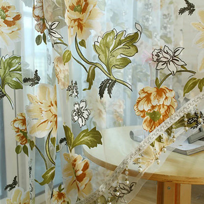 Zoom sur les motifs floraux jaunes et les finitions perlées d’un voilage transparent.