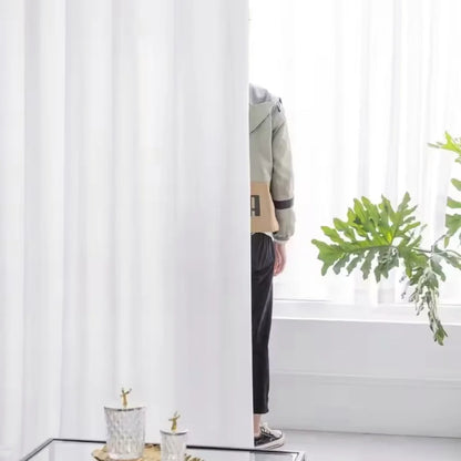 Voilage blanc en situation, partiellement ouvert, laissant deviner une silhouette derrière.