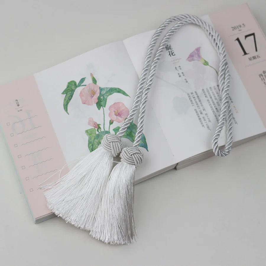 Embrasse rideau blanche avec cordon torsadé et pompons, posée sur un carnet, idéale pour une déco lumineuse.