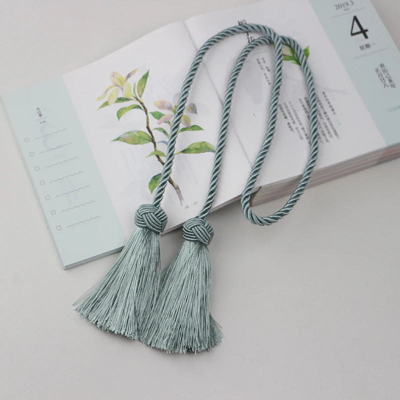 Embrasse rideau vert d’eau avec pompons sur carnet illustré, parfaite pour une ambiance douce et apaisante.