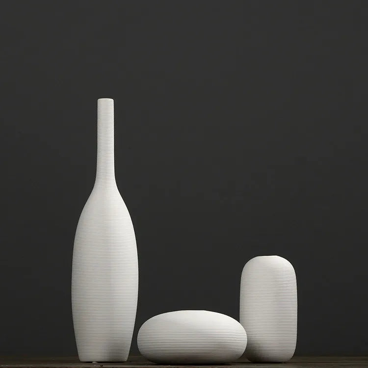Trois vases blancs élégants en forme épurée et contemporaine, disposés sur un fond sombre pour créer une atmosphère minimaliste et sophistiquée.