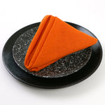Serviette en tissu orange vif sur une assiette noire avec des motifs texturés.
