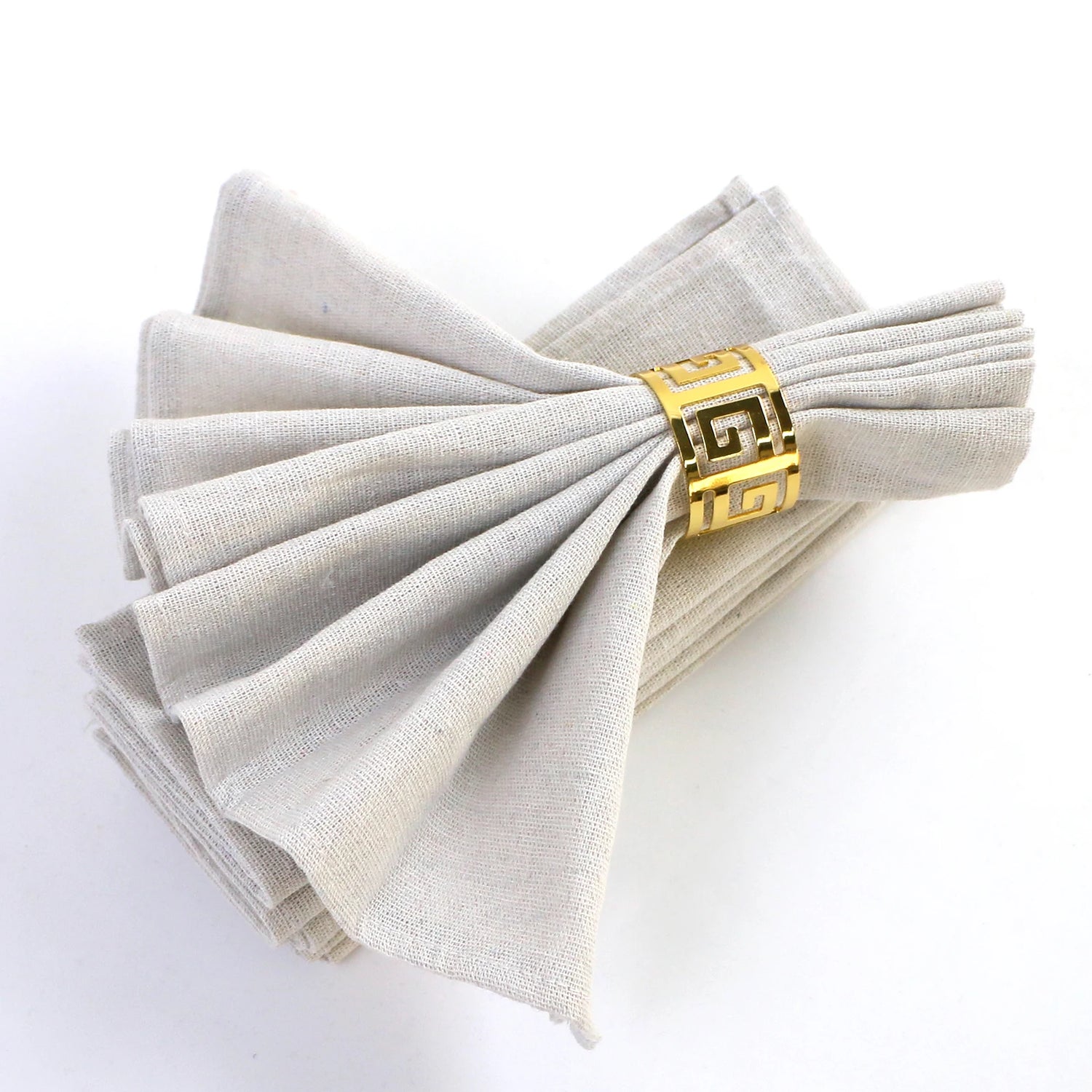 Serviettes pliées élégantes maintenues par un bracelet doré avec motif géométrique grec.