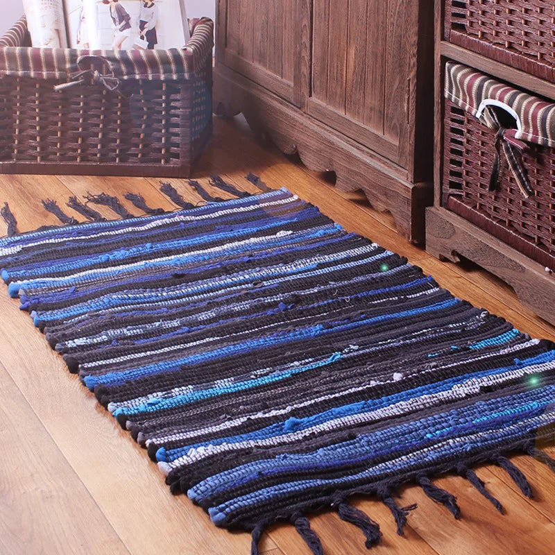 Tapis de sol en coton recyclé dans des tons bleus et noirs, avec des franges ornementales, placé sur un parquet en bois à proximité d'un panier en rotin.
