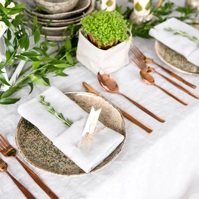 Composition élégante de vaisselle de table avec couverts en métal, plantes vertes et accessoires de décoration sur un fond blanc.