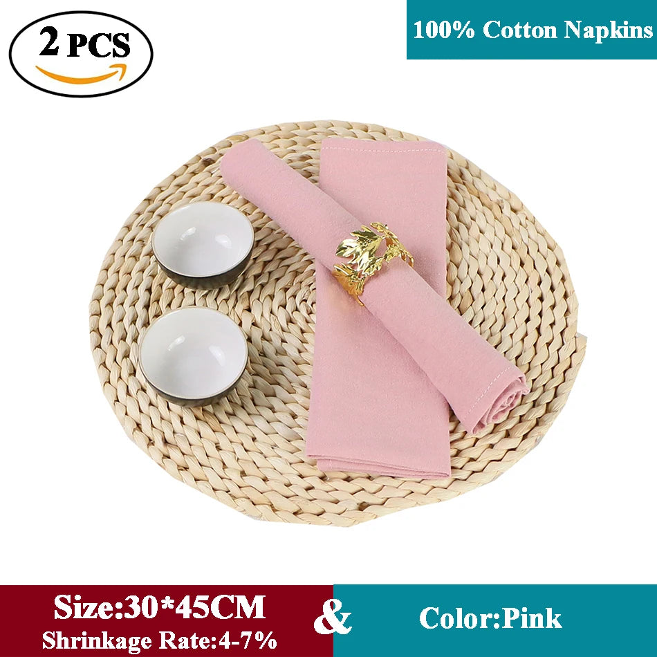 Serviettes en coton rose clair avec des détails dorés, posées sur un napperon en osier tressé.