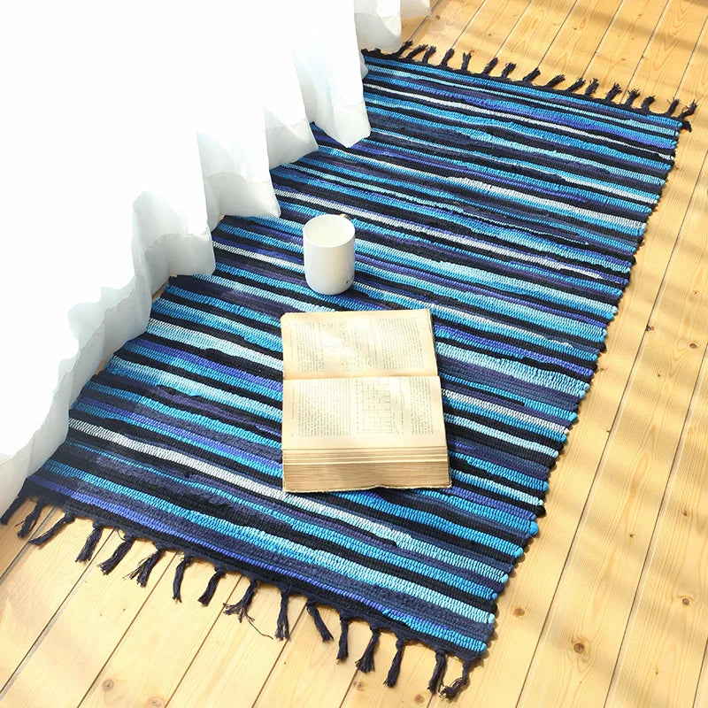 Ce tapis bleu et blanc rayé avec des franges sur un plancher de bois est un élément décoratif élégant et confortable pour créer une ambiance chaleureuse dans la pièce.