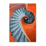 L'image représente un escalier en spirale avec des marches en métal de couleur grise sur fond orange, créant une impression graphique et géométrique.