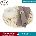 Des serviettes en coton marron de haute qualité, placées sur un support en osier, accompagnées d'une tasse blanche et d'un anneau décoratif.