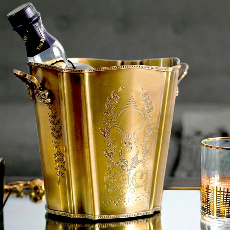 Le seau à glace doré, finement décoré de motifs floraux et de feuilles, présente une allure élégante et raffinée, parfaite pour rafraîchir une bouteille de vin ou de champagne lors d'un événement spécial.