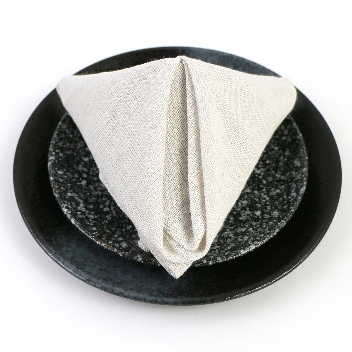 Une serviette blanche en tissu posée sur une assiette noire en pierre polie.