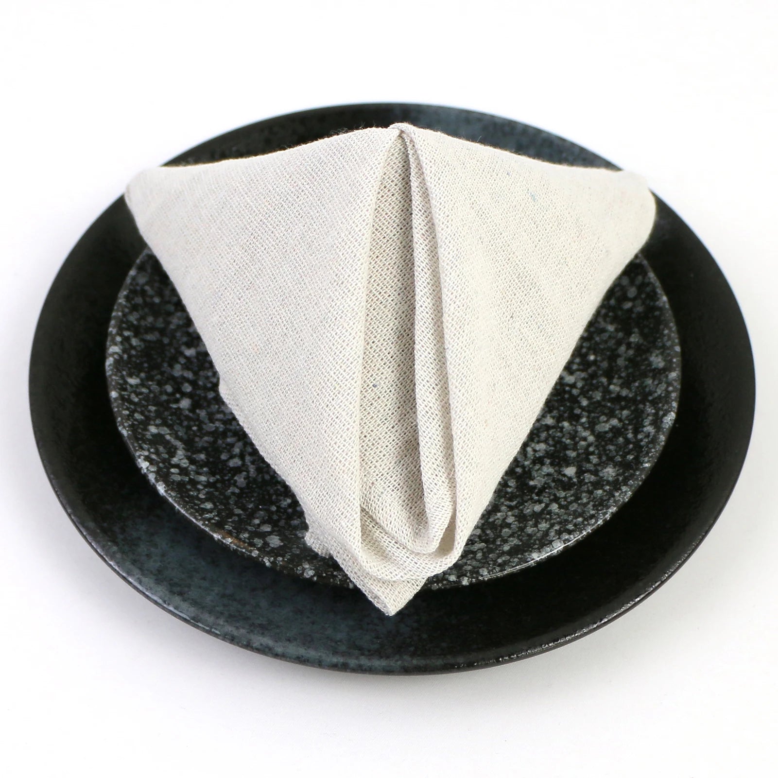 Une serviette blanche en tissu posée sur une assiette noire en pierre polie.